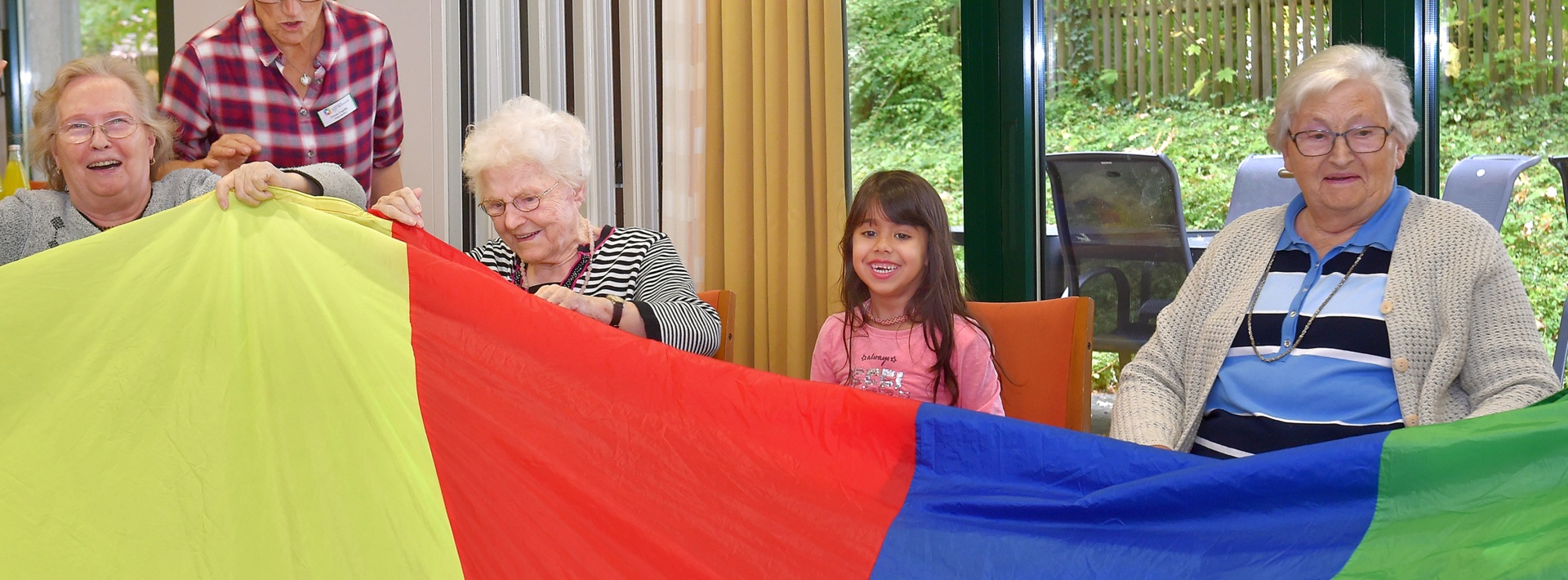 Seniorinnen und ein Mädchen lächeln und halten eine bunte große Flagge