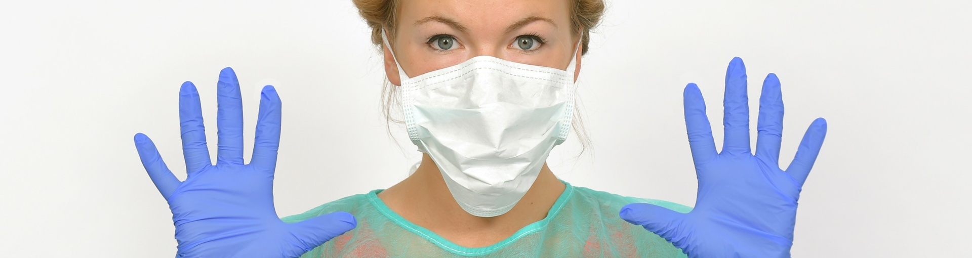 Junge Dame in medizinischer Schutzkleidung trägt Maske und zeigt ihre Hände mit Handschuhe bedeckt